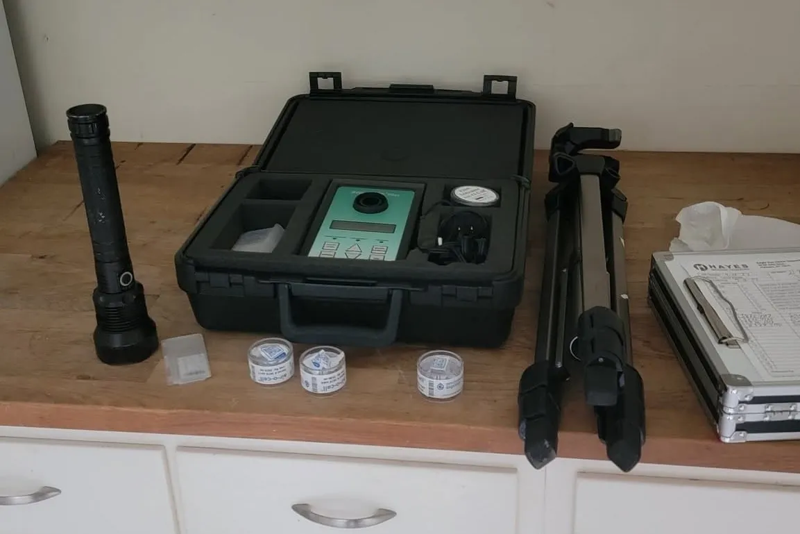 Mold assessment equipment laid out on a counter: an air sampling pump in its case, spore trap cassettes, a tripod and a flashlight