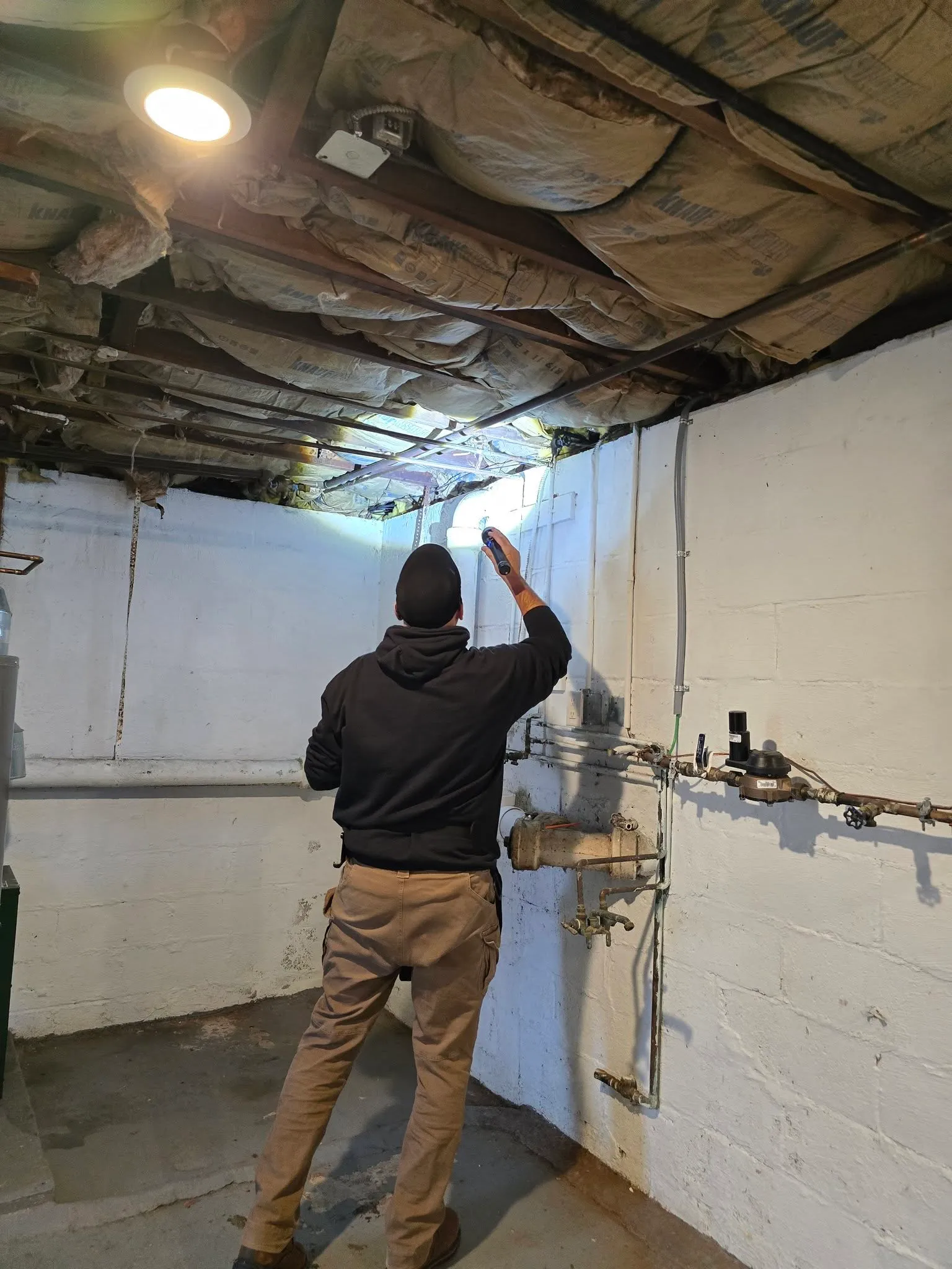 Eagle Eye inspector Lance Kotash using a flashlight to inspect an exposed basement ceiling